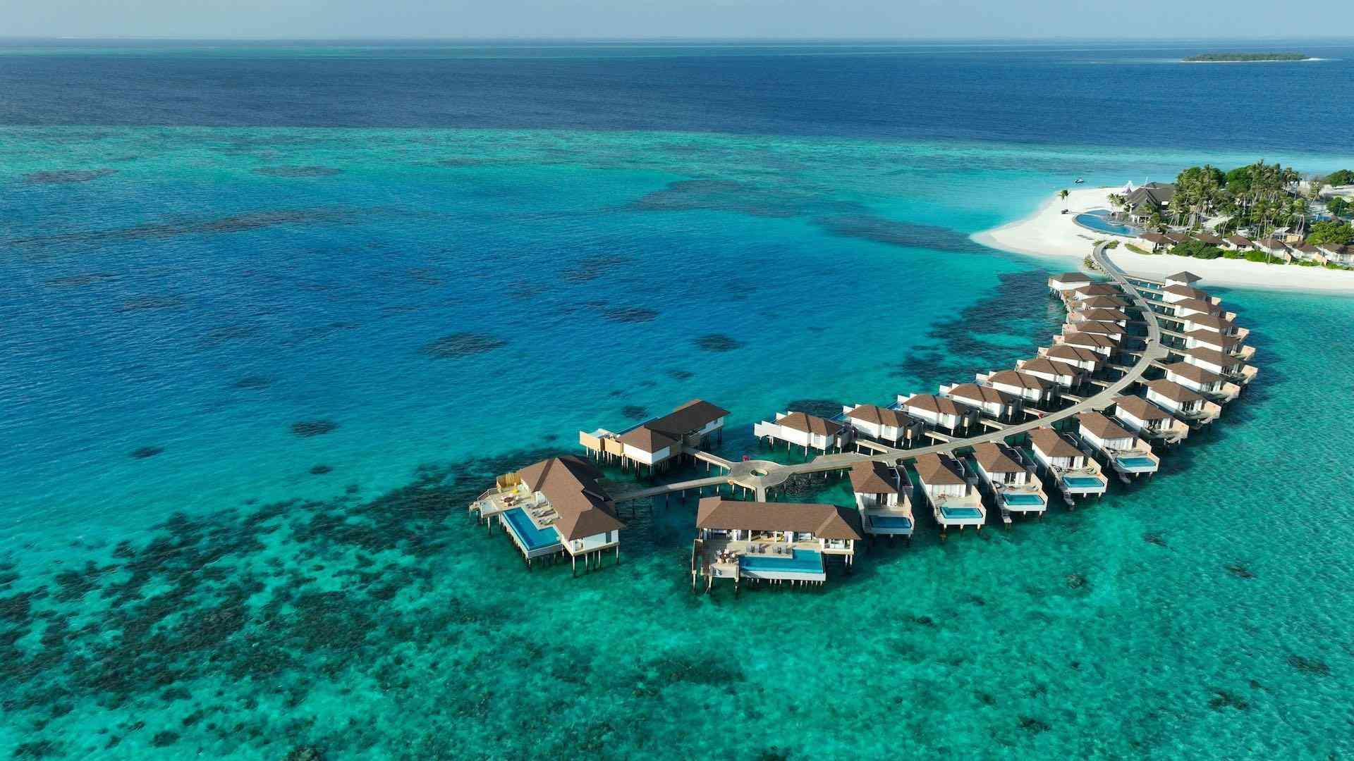 Luxuriöse Überwasserbungalows auf türkisfarbenem Meer bei tropischer Insel, ideal für Urlaub.