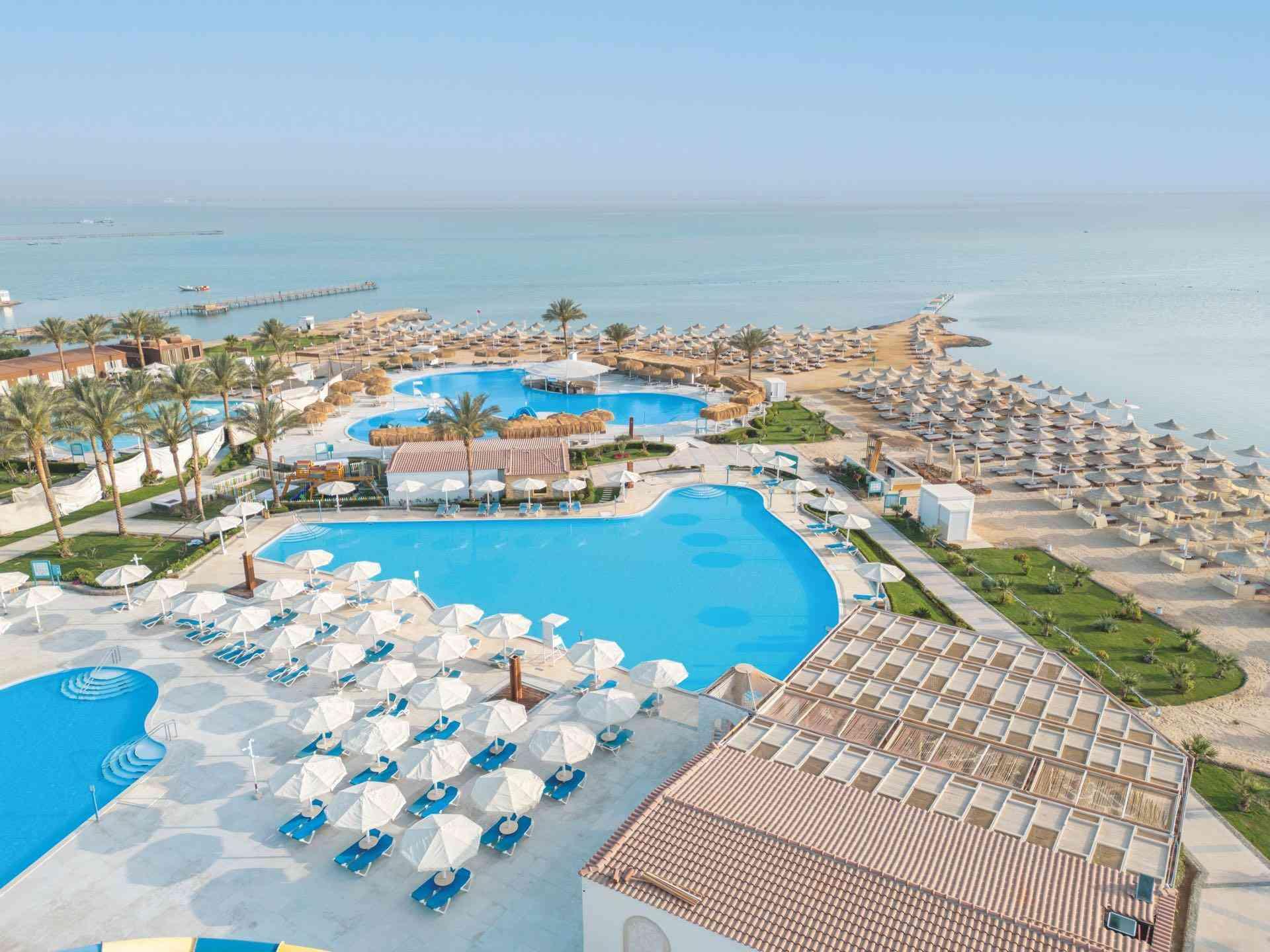 Große Hotelanlage mit mehreren Poolbereichen, Sonnenschirmen und direktem Zugang zum Strand.