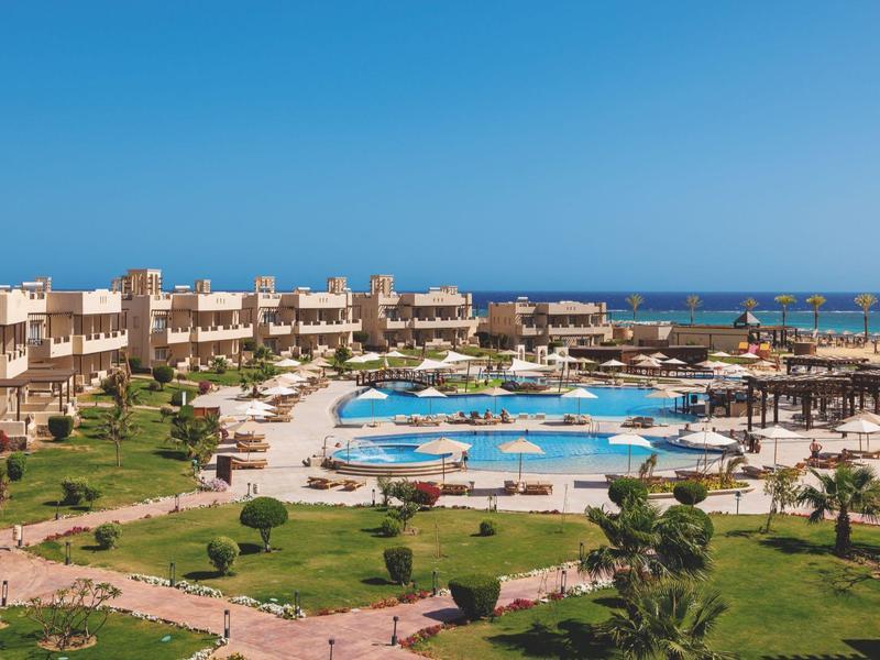 Großes Hotelresort mit mehreren Pools, Liegestühlen und Palmen, direkt am Meer unter blauem Himmel.