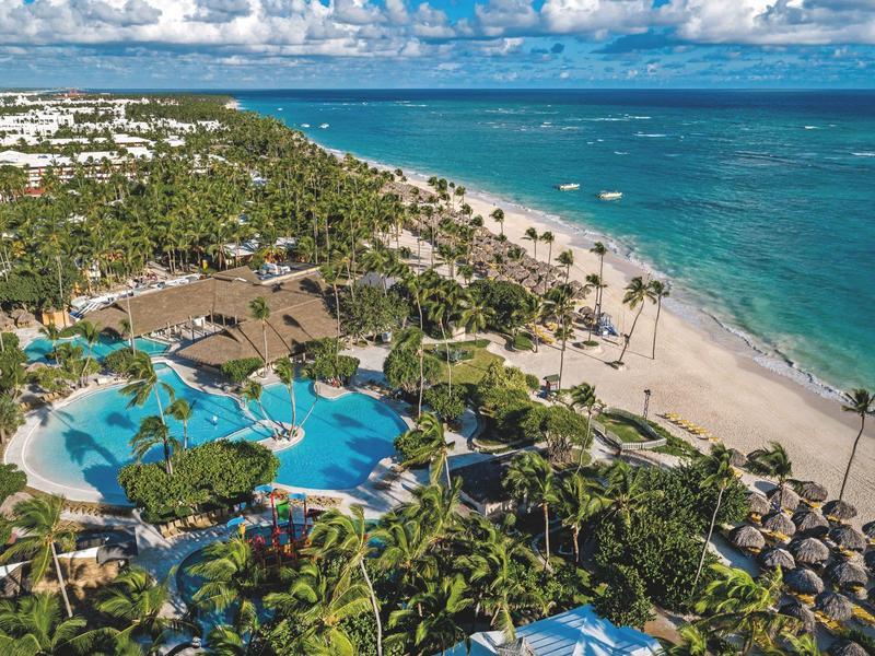 Luxuriöses Strandhotel mit großen Poolanlagen, Palmen und feinem Sandstrand am türkisblauen Meer.