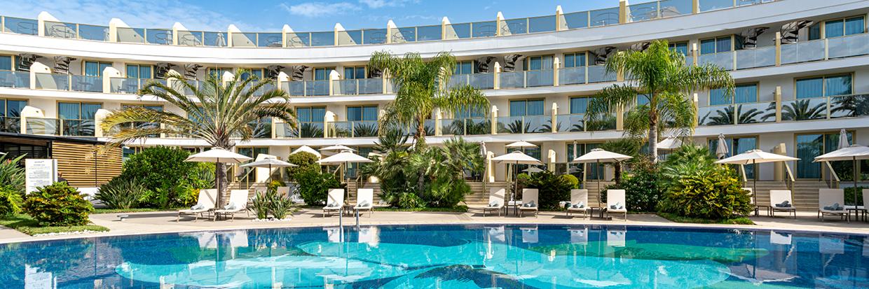 Hotel mit rundem, weißem Gebäude, Palmen und klarem blauen Pool für entspannte Urlaubstage.