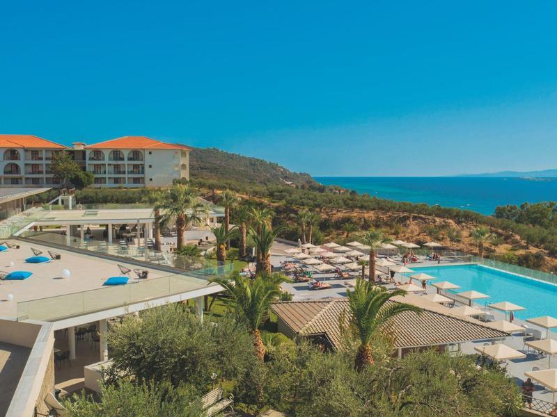 Luxushotel mit Pool, Sonnenliegen und Blick auf das Meer in einer sonnigen Küstenlandschaft.