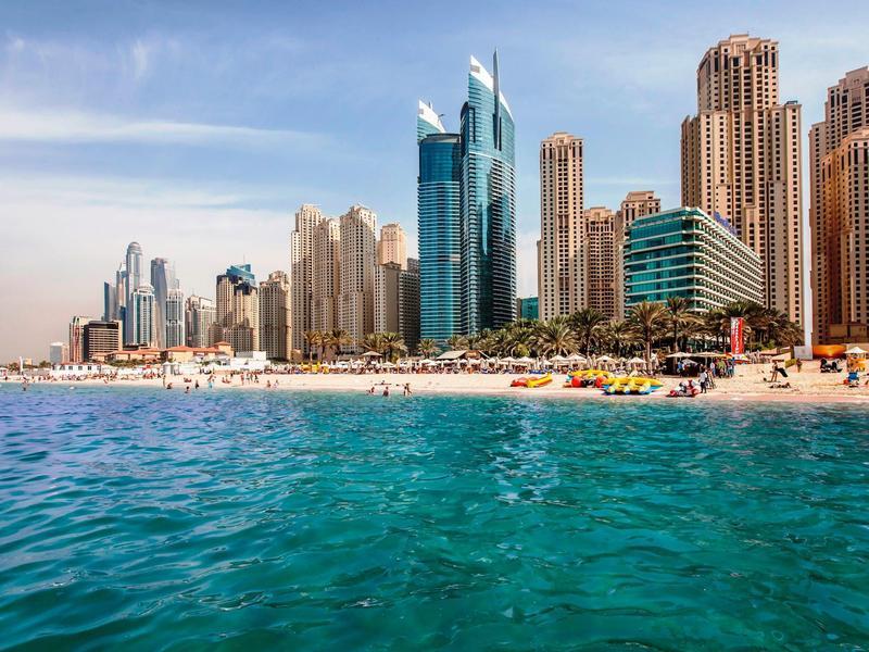 Strand mit klarem blauen Wasser vor moderner Skyline aus hohen Hotels und Wohngebäuden bei Sonnenschein.