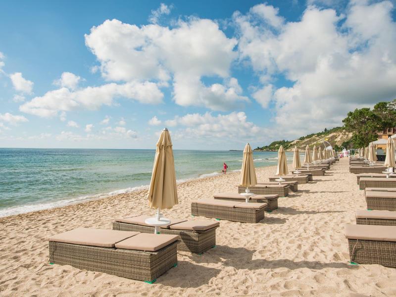 Sandstrand mit Liegen und geschlossenen Sonnenschirmen, ruhiges Meer und bewölkter Himmel.