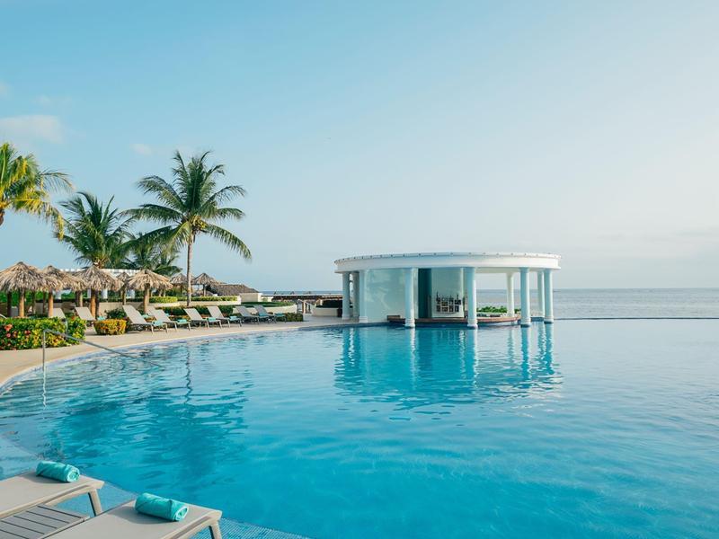 Infinity-Pool mit Bar, Liegen und Palmen, umgeben von ruhiger Meereskulisse bei Hotelanlage.
