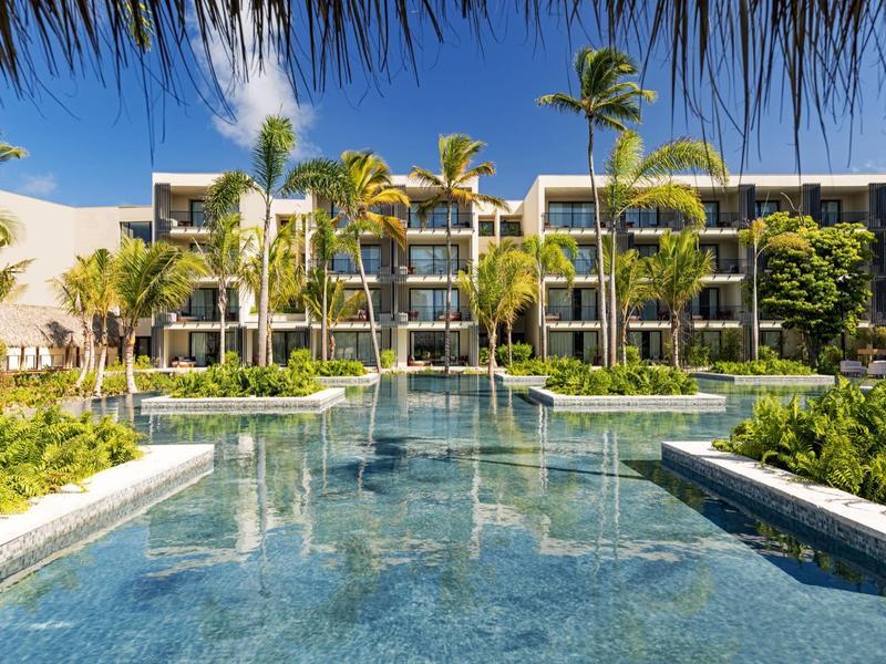 Moderner Hotelkomplex mit großem Pool, umgeben von Palmen und klar blauer Himmel im Hintergrund.