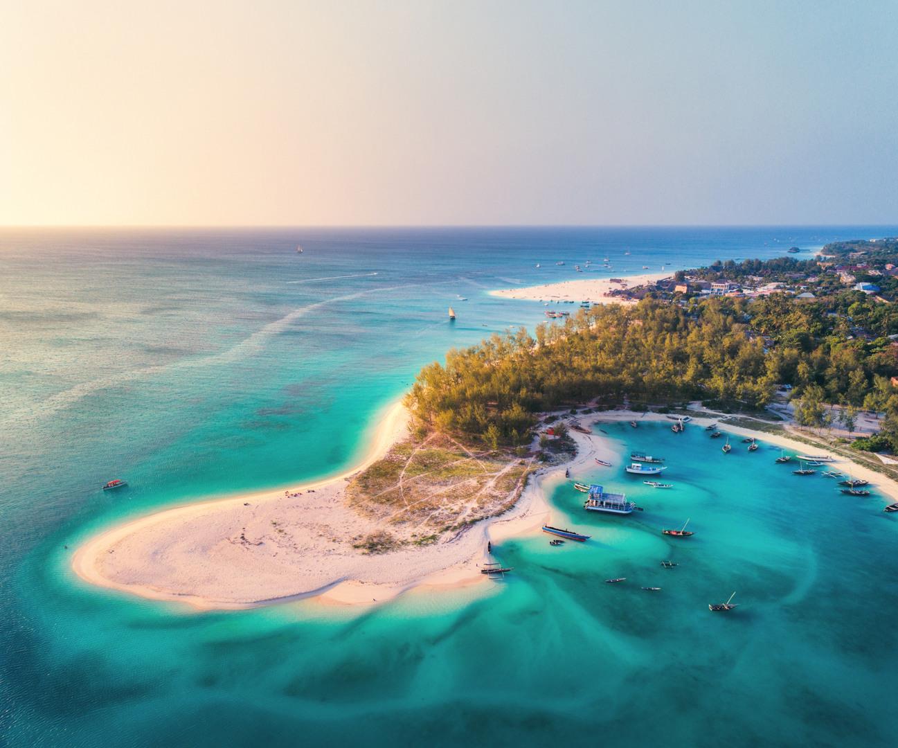 Insel mit weißem Sandstrand, türkisfarbenem Wasser und kleinen Booten, idealer Urlaubsort am Meer.