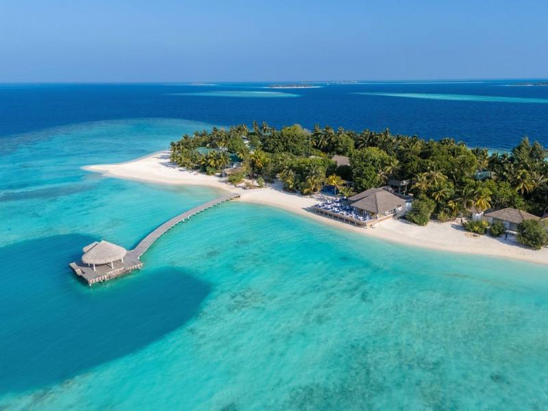 Tropische Insel mit weißem Sandstrand, türkisfarbenem Wasser und Resort mit Steg und Bungalows.