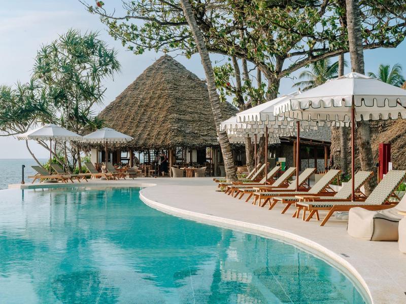 Luxuriöser Hotelpool mit weißen Liegestühlen und Sonnenschirmen, exotische Pflanzen und Meerblick.