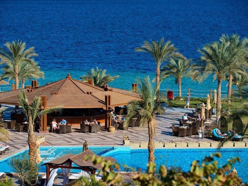 Ein ruhiger Hotelpool mit Bar, Palmen und Blick auf das tiefe blaue Meer.