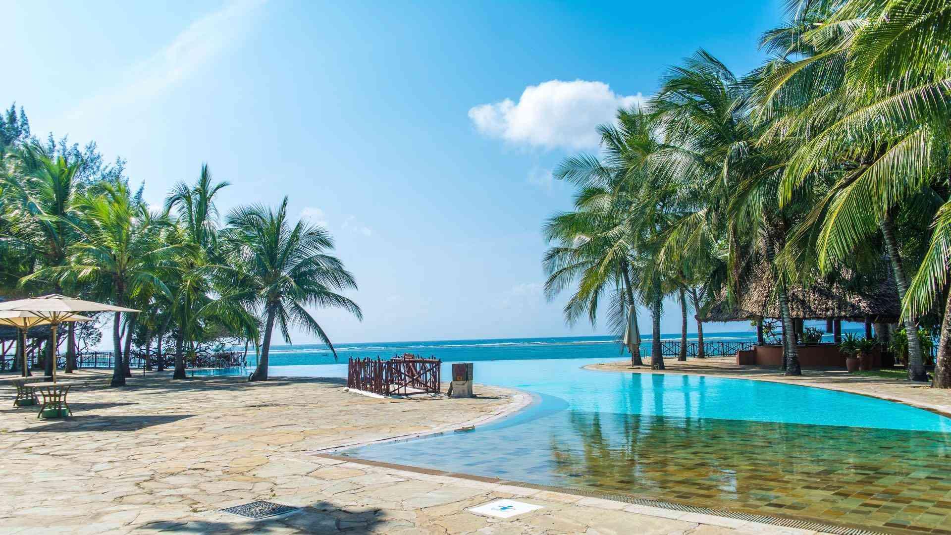 Sonniger Poolbereich mit Palmen und Blick auf den blauen Ozean, ideal für einen tropischen Urlaub.