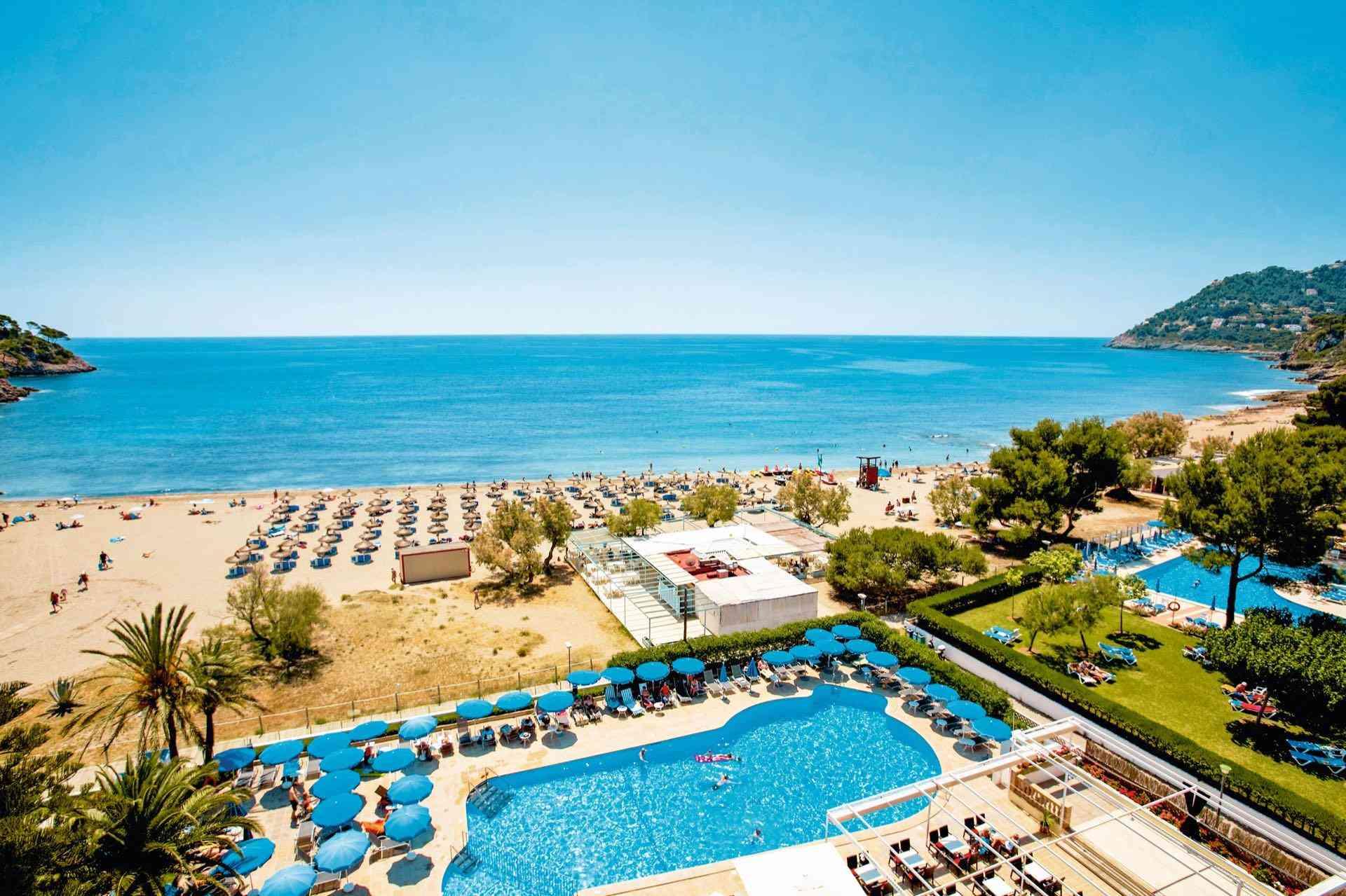 Hotelpool mit Sonnenliegen, Sandstrand und ruhigem blauem Meer am klaren Himmel.