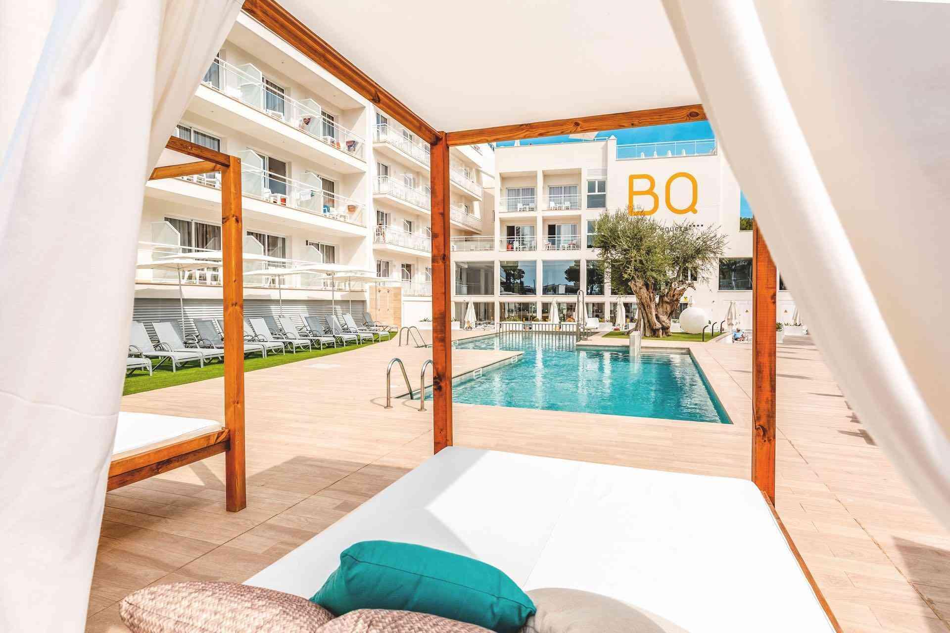 Moderner Hotelpool mit Liegestühlen und Pavillon, umgeben von weißen Gebäuden und grüner Wiese.
