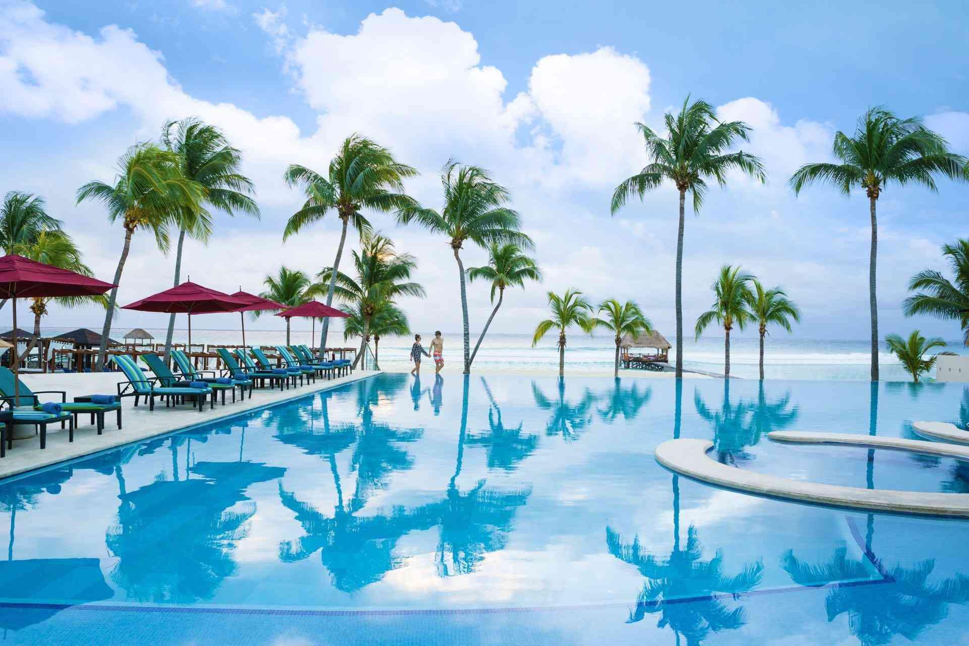 Luxuriöser Hotelpool mit Palmen, blauen Liegestühlen und Blick auf das ruhige Meer.