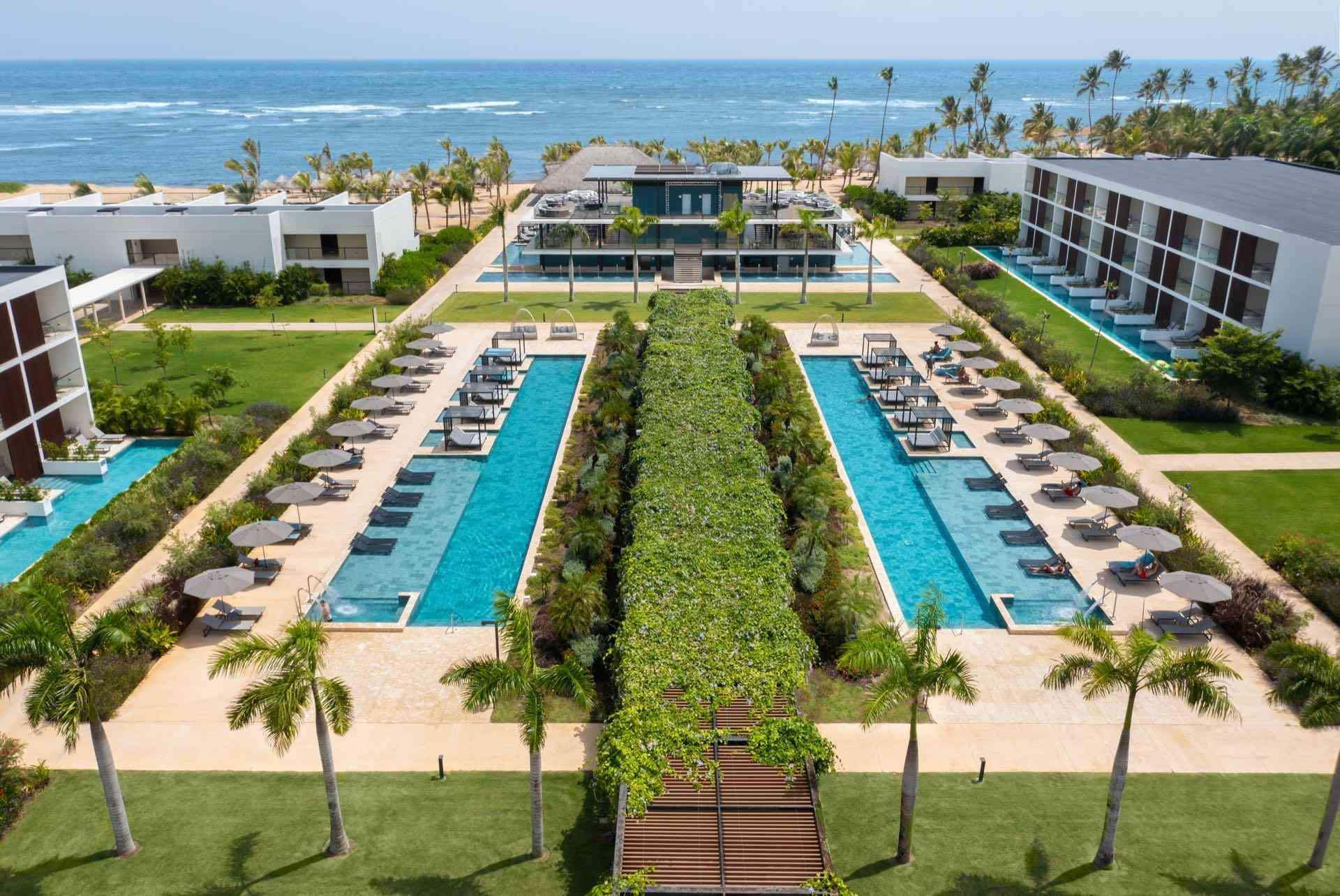 Luxuriöses Strandhotel mit zwei langen Pools, Palmen und direktem Meerblick in tropischer Umgebung.