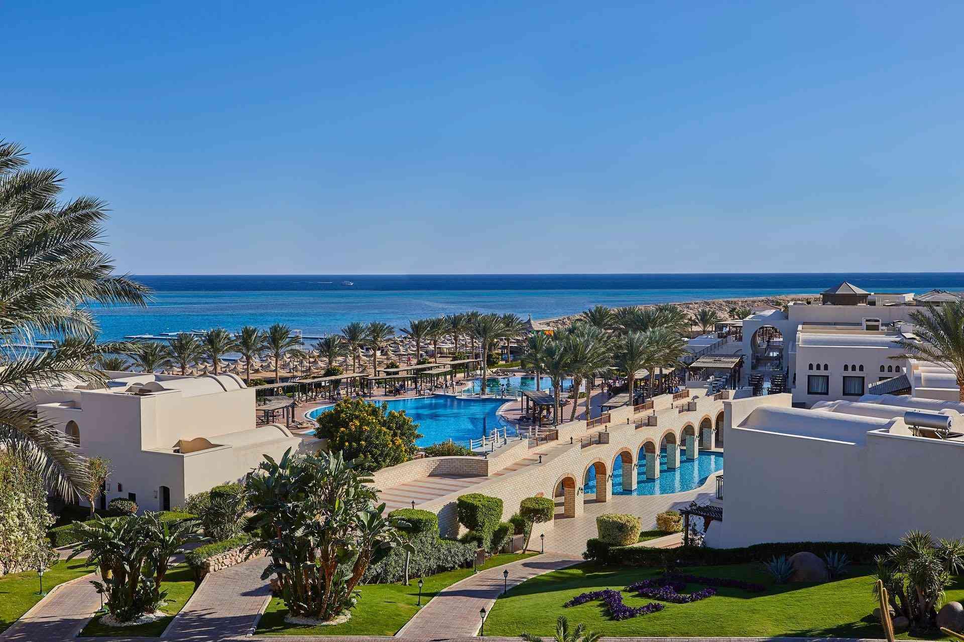 Luxuriöses Hotel am Meer mit großem Pool, Palmen und klarem blauem Himmel bei sonnigem Wetter.
