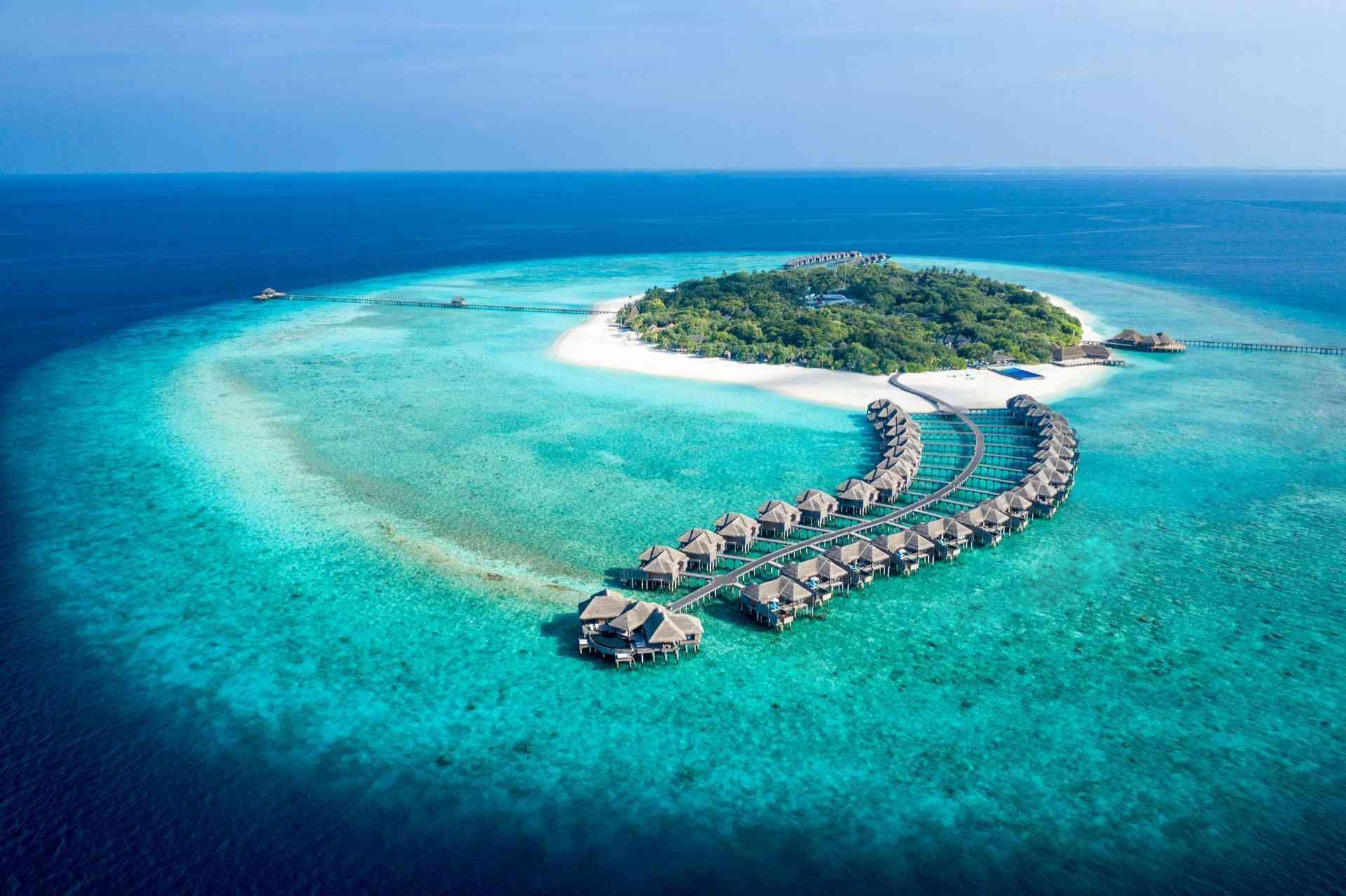Tropische Insel mit Überwasserbungalows, blauem Meer und strahlendem Himmel, ideal für Urlaub.