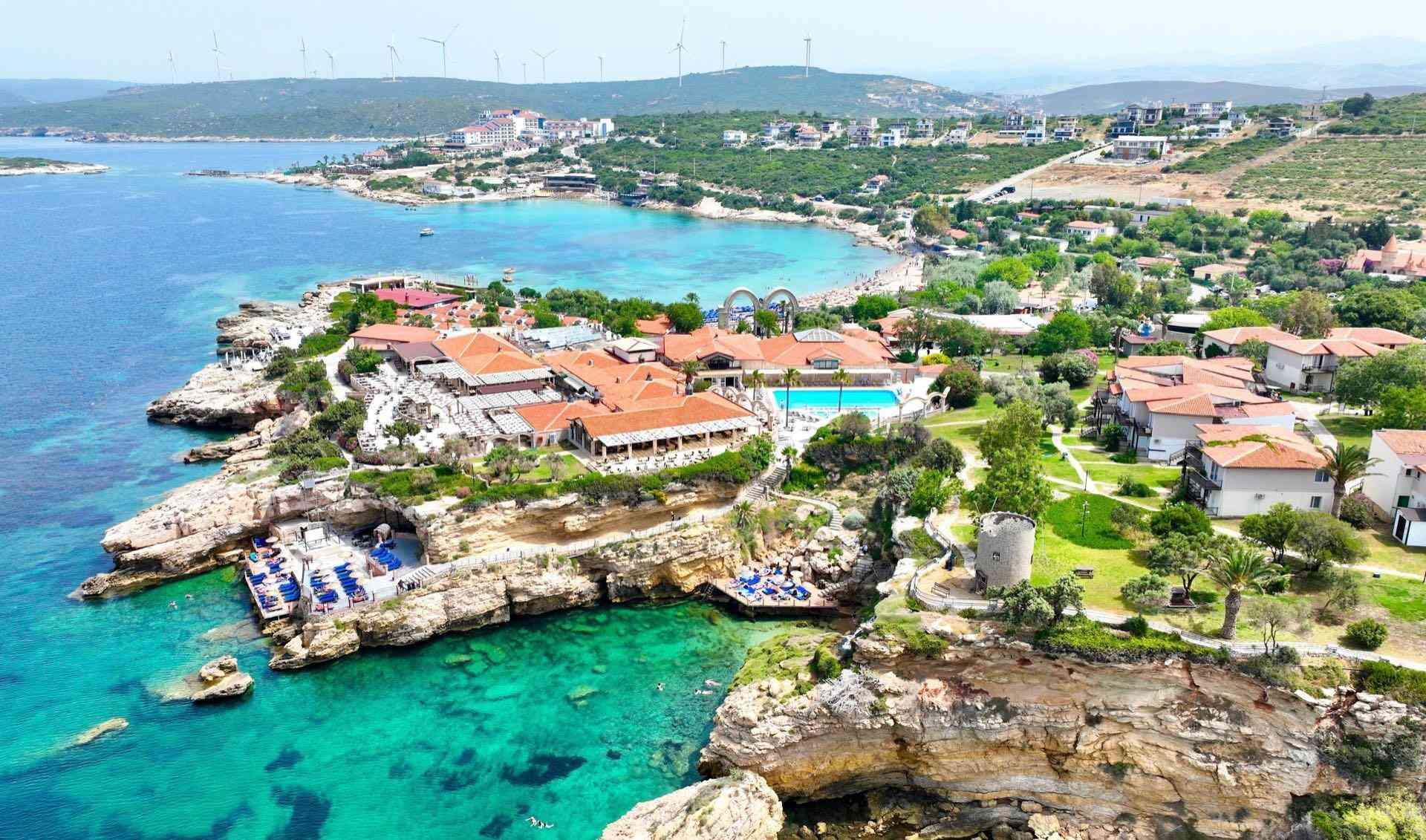 Hotelanlage mit Pool auf felsiger Küste, türkisfarbenes Meer und grünes, hügeliges Umland.