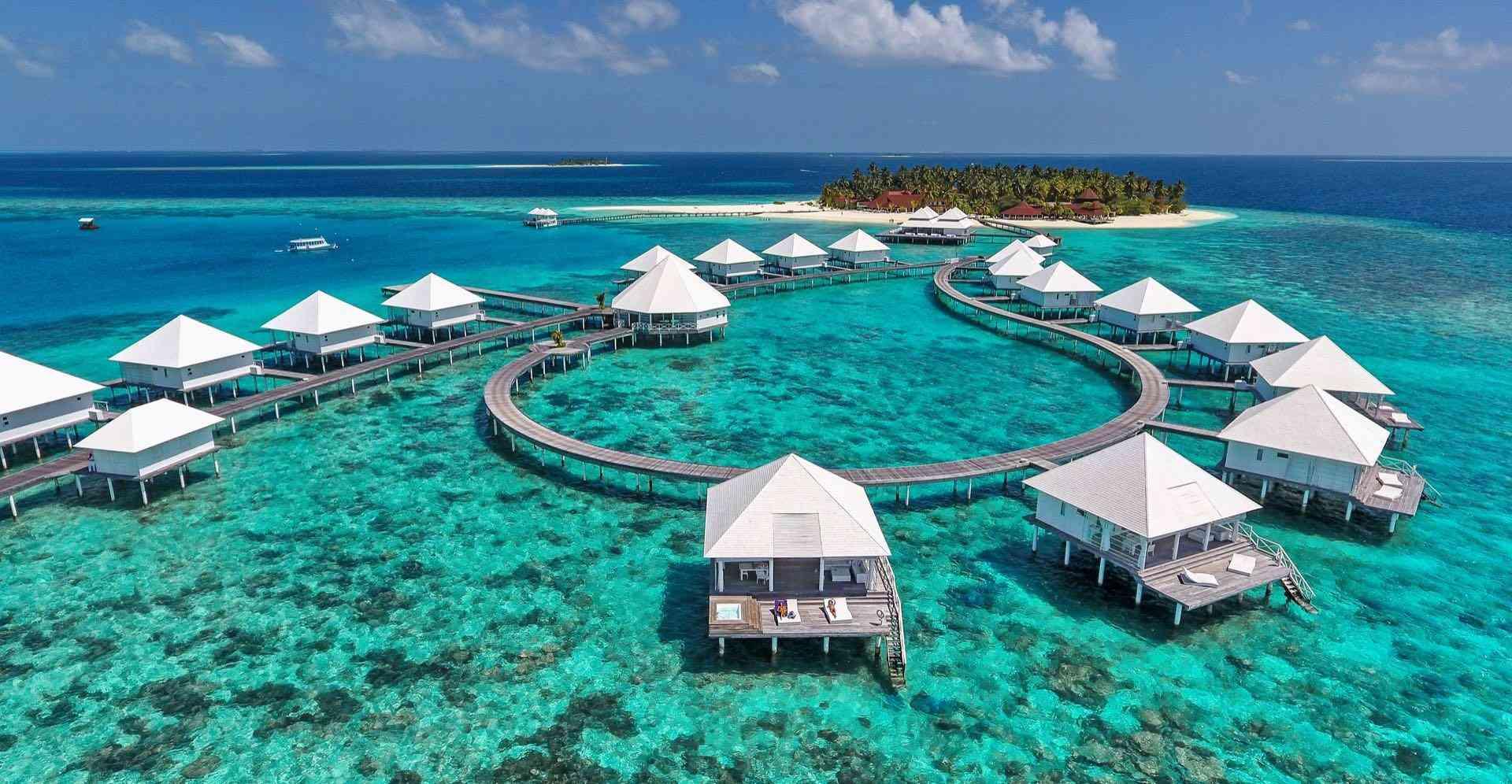 Überwasser-Bungalows mit weißen Dächern umgeben von klarem türkisfarbenem Wasser und kleiner Insel.