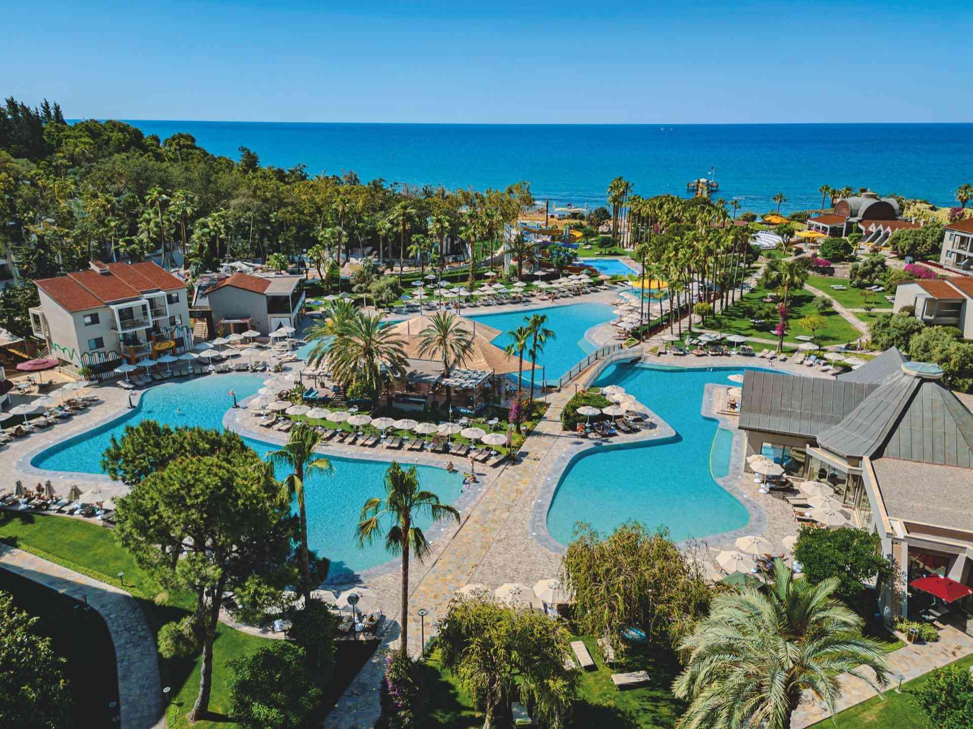 Luxuriöses Hotelresort mit großen, verschlungenen Pools, Palmen und direktem Meerblick unter klarem Himmel.