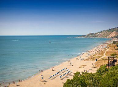 Breiter Sandstrand mit Sonnenliegen und sanftem Wellengang lädt zum entspannten Urlaub am Meer ein.