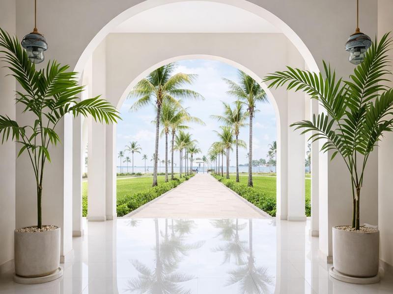 Heller Hotelgang mit Palmen, weißem Marmor und Blick auf exotischen Garten und Meer.