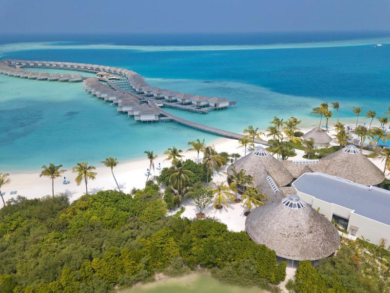 Luxuriöse Überwasser-Bungalows, weißer Sandstrand und türkisfarbenes Meer an tropischem Urlaubsort.