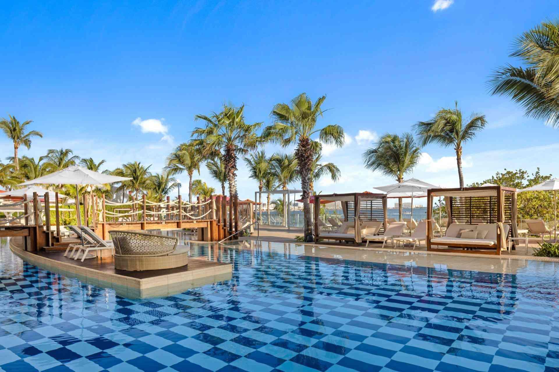Moderner Poolbereich mit Sonnenbetten, Palmen und blauem Himmel in einem Hotelresort.