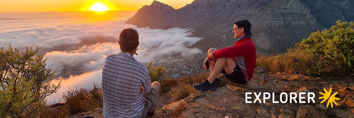Zwei Personen genießen den Sonnenuntergang über Nebel und Bergen, entspannte Atmosphäre am Reiseziel.