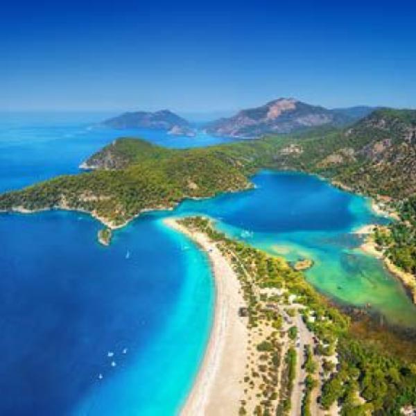 Türkisblaue Lagune mit weißem Sandstrand umgeben von grünen Hügeln, ideal für Urlaub und Entspannung.