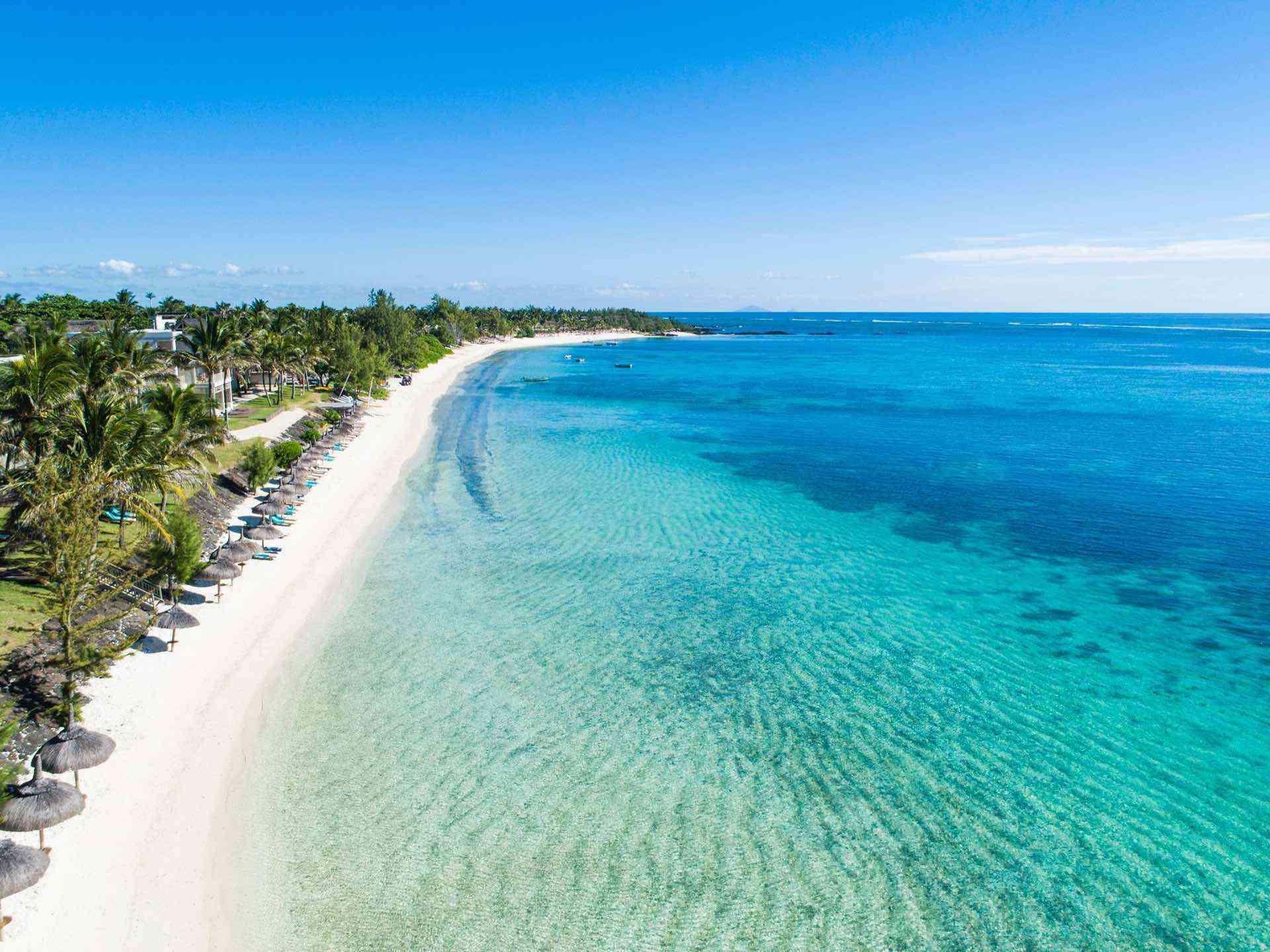 Langer weißer Sandstrand mit Palmen und klarem, türkisblauem Wasser für erholsamen Urlaub.