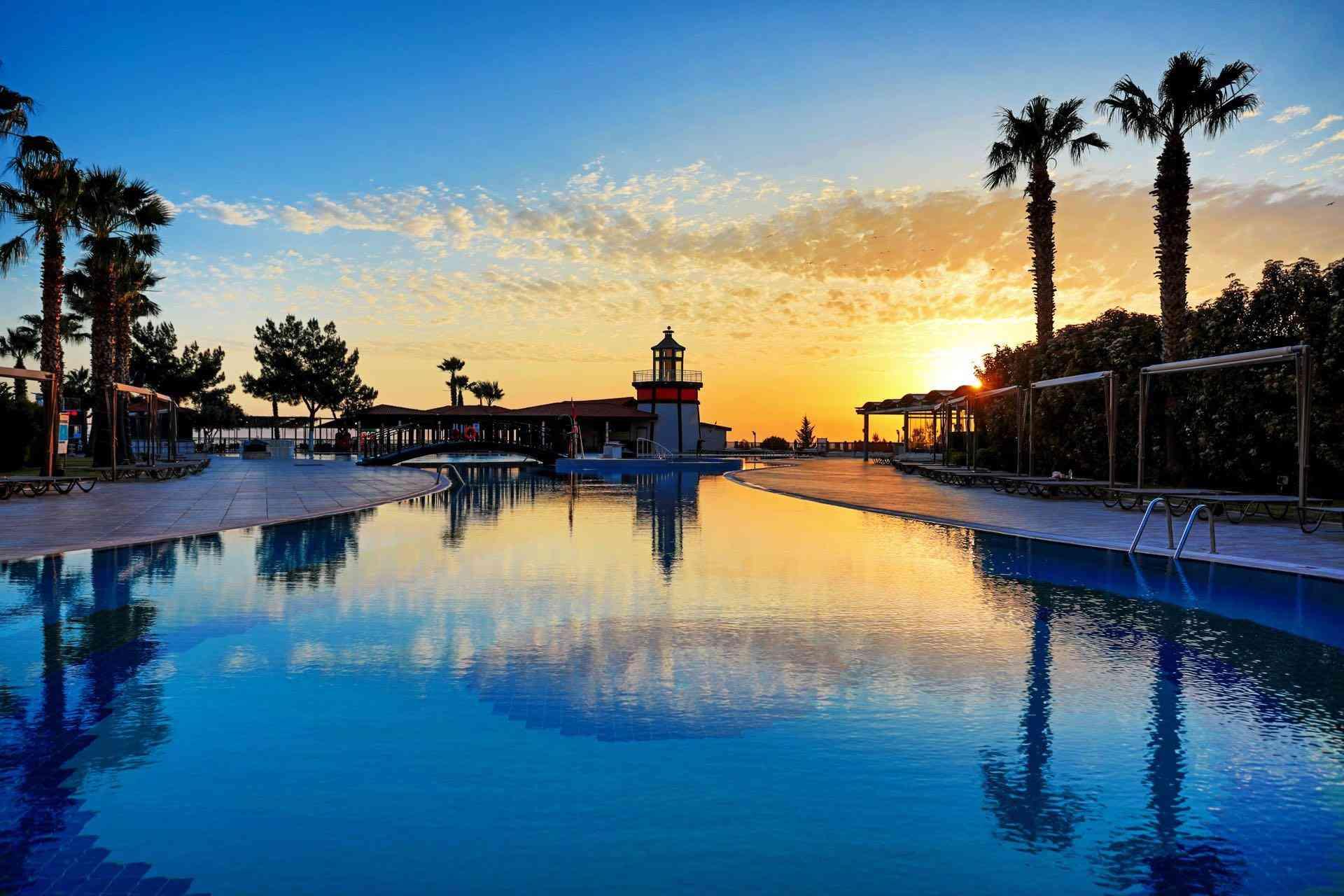 Luxuriöser Hotelpool bei Sonnenuntergang, umgeben von Palmen und entspannenden Liegeplätzen.