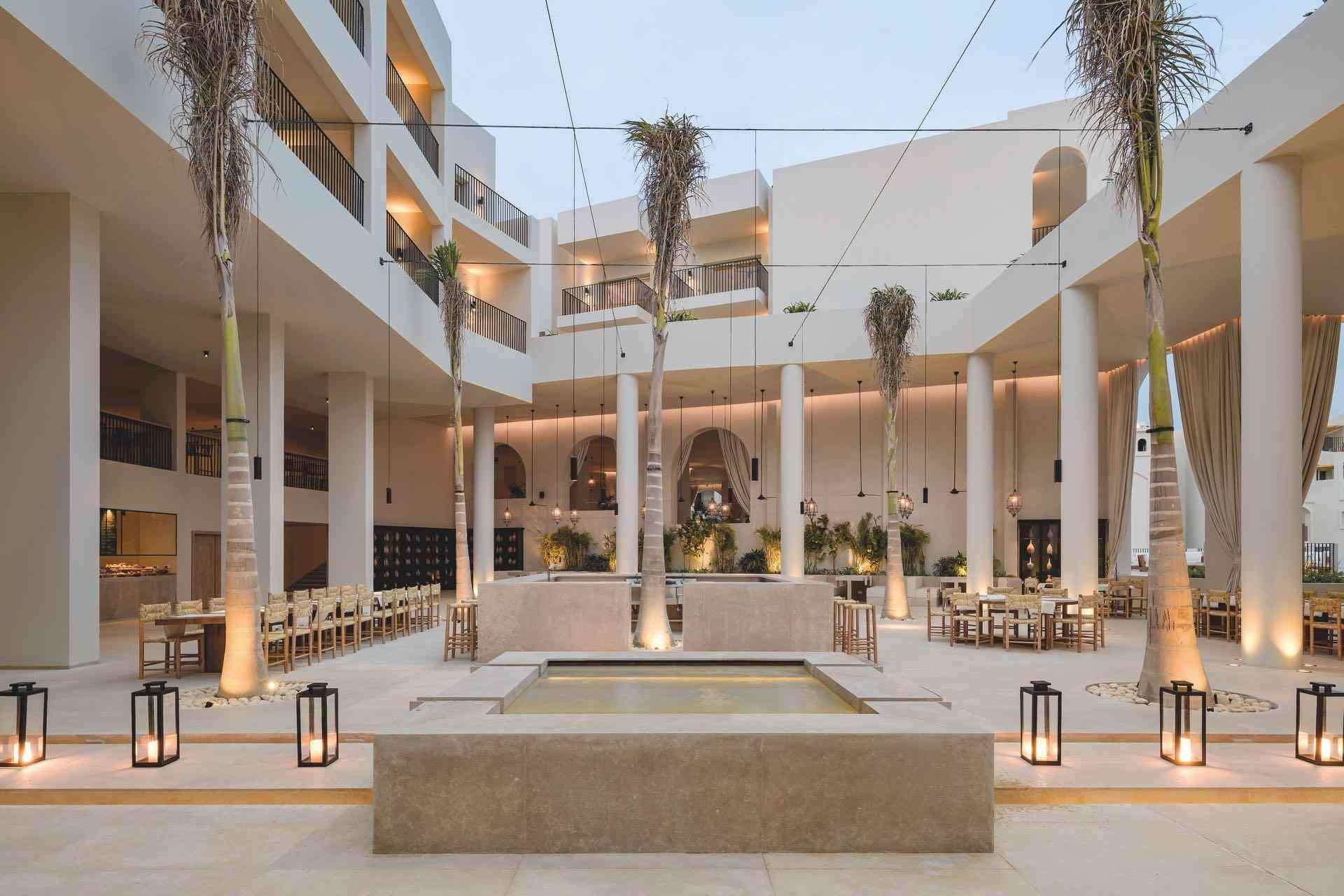 Moderner Hotelinnenhof mit quadratischem Wasserbecken, Palmen und stilvoller indirekter Beleuchtung.